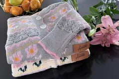 Saco de punto con diseño floral, cuello redondo y cierre frontal con botones. Presenta detalles de tejido calado en las mangas y puños acanalados. Incluye etiqueta de cuero sintético con la marca Amante.