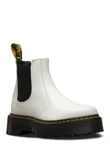 Botas Chelsea de plataforma Dr. Martens modelo 2976 Quad, confeccionadas en cuero liso color blanco. Presentan paneles elásticos laterales en color negro, suela de plataforma dentada tipo comando con costuras amarillas características y tirador trasero con logo de la marca.
