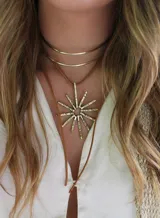 Collar con colgante dorado en forma de sol y tira de cuero sintético marrón.