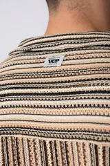 Camisa de manga corta con cuello solapa, corte holgado y cierre frontal de botones. Presenta un diseño de rayas verticales en tonos beige, negro y blanco.