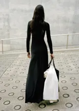 Vestido largo negro de manga larga, con escote redondo y diseño ajustado que se ensancha levemente hacia el suelo.