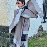 Ruana de material símil cachemira, de diseño bicolor en tonos gris y lila con bandas anchas en los bordes.