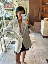 Blazer oversize bicolor de la marca Agnés, con diseño de doble faz que combina un lado en tejido gris oscuro liso y otro lado en tejido tostado con patrón de rayas diplomáticas. Cuenta con solapas clásicas, cierre frontal de dos botones y bolsillos aplicados.