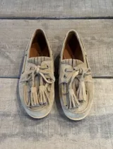 Mocasín náutico de gamuza color camel, con detalle de flecos y borlas en el empeine, cordones decorativos y suela plana.