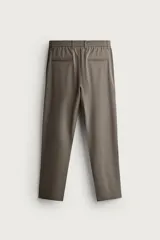 Pantalón de corte slim fit y color negro, confeccionado en tejido elástico. Cuenta con cintura elástica, trabillas, bolsillos frontales y cierre con cremallera y botón.