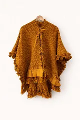 Ruana de punto color mostaza con textura, cuello con volados y lazo frontal ajustable. Presenta detalles de volados aplicados en lino en las mangas y el ruedo, finalizando con flecos artesanales.