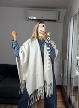 Poncho de tejido suave color blanco, con diseño abierto y flecos en el ruedo inferior.