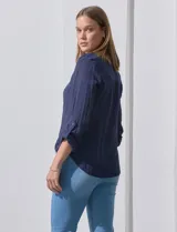 Blusa blanca de gasa marca Zac & Rachel, con cuello a la base, escote en V, abertura central con botones, bolsillo aplicado en el pecho y mangas largas regulables con presilla y botón. Tiene terminación opcional de nudo en el ruedo.