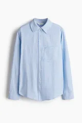 Camisa en tejido liviano de mezcla de lino y viscosa, a rayas celestes y blancas, con cuello, botones delanteros y bolsillo superior abierto. Modelo de manga larga con puños abotonados y bajo redondeado.
