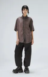 Camisa de corte oversize y mangas cortas, confeccionada en tela con efecto de teñido artesanal maltinto en tono gris. Presenta cuello clásico, cierre frontal con botones y costuras verticales decorativas en el frente.