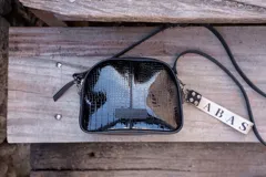 Bandolera pequeña de cuero negro con textura tipo cocodrilo, correa larga ajustable y llavero con el logo de la marca.