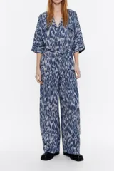 Mono largo de viscosa con estampado abstracto en tonos azules y grises. Tiene cuello camisero con solapa, manga corta murciélago con fruncidos en los hombros, cierre frontal con cremallera oculta, bolsillos con tapeta redondeada en el pecho y con fuelle en la cadera, y cinturón de tela.