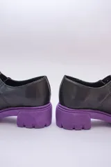 Guillermina de cuero negra con suela tractorada roja y hebilla dorada.