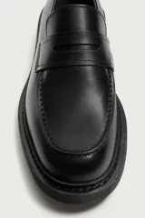 Mocasín de piel color negro, con diseño superior liso, detalle de antifaz en el empeine, horma redonda y suela track dentada.