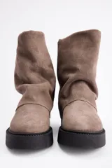 Bota de caña media confeccionada en cuero vacuno color marrón oscuro, con diseño de pliegues en la caña y suela de goma al tono con textura estriada.