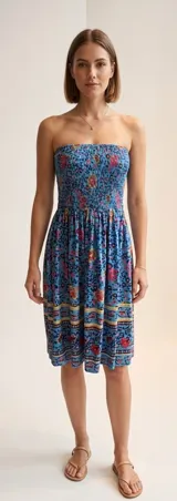 Vestido strapless de largo midi con cuerpo fruncido elástico y falda fluida. Presenta un estampado floral multicolor sobre fondo azul con detalles de guardas decorativas en el ruedo.