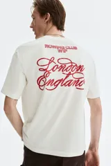 Remera boxy de algodón color blanco, con cuello redondo acanalado, mangas cortas y hombros caídos. Presenta un pequeño estampado rojo en el pecho con las inscripciones 'ROWING CLUB W1F'.