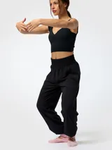 Pantalón de microfibra negro, de corte estilo bombacho y silueta relajada, con cintura y puños elásticos fruncidos. Presenta costuras frontales verticales y bolsillos funcionales.