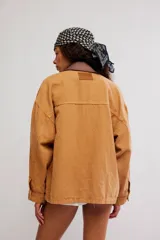 Campera oversize de denim en color marrón, con hombro caído, cuello de lona marrón en contraste, bolsillos frontales con solapa, cierre de botones metálicos y puños abotonados.