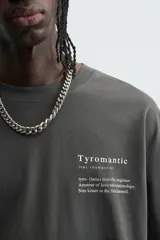 Camiseta de manga corta y cuello redondo, color gris oscuro o negro deslavado, con estampado de texto en blanco en el pecho.