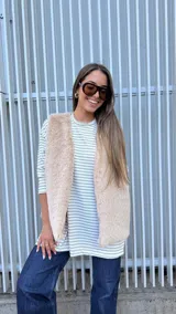 Chaleco de piel sintética en color beige, con diseño sin mangas, corte recto y silueta amplia. Cuenta con forro interior y bolsillos laterales.