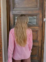 Camisa de manga larga con estampado de rayas verticales en color rojo y blanco. Presenta cuello alto con volados, cierre frontal con botones y detalles de volados en la solapa y en los puños.