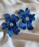 Par de aros con diseño de orquídeas azules con glitter y centro de pedrería plateada.