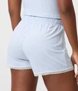 Short de pijama celeste de peach touch con estampa de moñitas blancas, cintura elastizada con bragueta frontal de botones y detalle de encaje blanco en los bajos.