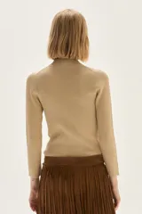 Polera de tejido de punto acanalado en color beige, con cuello alto y mangas largas. Presenta un sutil acabado brillante gracias a sus detalles en lurex.