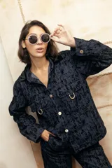 Camisa recta de gabardina con efecto "roto", que aporta volumen y textura. Presenta bolsillos amplios con solapa en el frente adornados con mini estribos dorados y cierre frontal de botones.