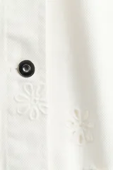 Campera corta de sarga de algodón blanca con detalles de broderie en forma de flores, cuello mao, cierre frontal con botones y bolsillos de parche delanteros.