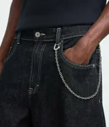 Pantalón de jean estilo baggy balloon, de corte holgado con volumen en las piernas y cintura fija con trabillas. Presenta costuras a contratono y detalle de cadena metálica lateral.