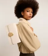 Cartera tipo shoulder bag de tamaño mediano, confeccionada en poliuretano color marrón oscuro. Presenta una solapa frontal con un detalle metálico dorado de forma orgánica y asa ajustable.