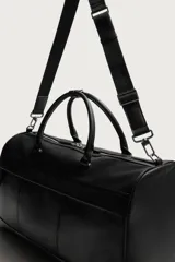 Bolso de viaje de diseño estructurado en color negro con acabado grabado. Cuenta con compartimento principal con cierre de cremallera, bolsillo frontal con cierre y asas de mano reforzadas. Incluye correa de hombro ajustable y extraíble.