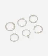 Kit de seis anillos de metal en tono plateado con texturas variadas, incluyendo un modelo con piedra de zirconia en forma de gota y otros diseños lisos y ondulados.