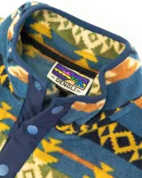Buzo polar de cuello alto con cierre frontal de botones a presión, confeccionado en fleece sintético. Presenta un estampado geométrico multicolor con predominancia de tonos azules, amarillos y verdes. Incluye un bolsillo frontal tipo cargo con solapa y cierre de botón, además de bolsillos laterales ocultos.