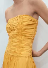 Top bandeau amarillo con diseño fruncido en el cuerpo, sin mangas y cierre de cremallera en la espalda.