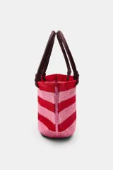 Bolso tipo cesto de yute con diseño de rayas horizontales en tonos rojo y rosado, asas de mano de cuero en color marrón oscuro y base redondeada.