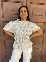 Blusa a cuadros crema con bordado floral tono sobre tono, cuello alto con volado, mangas cortas abullonadas, frunces frontales y lazos laterales regulables.