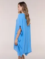 Vestido playero tipo túnica de corte holgado color rosado, confeccionado en tejido semi transparente con textura sutilmente arrugada. Cuenta con escote en V pronunciado, mangas estilo kimono de caída fluida y aberturas laterales en el ruedo irregular.
