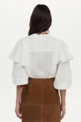Camisa blanca de lino con cuello mao, volados en los hombros y mangas abullonadas con elástico. Cierre frontal con botones.