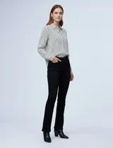 Camisa de manga larga, color blanco y negro, con cuello con solapa y abertura central con botones ocultos. Presenta un estampado geométrico repetitivo.