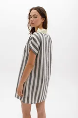Vestido corto con rayas verticales y horizontales en tonos grises y blancos, con volados color lima en el escote y cierre frontal con botones.