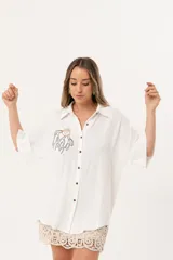 Camisa blanca de silueta oversize, con cuello camisero, manga 3/4 y corte más largo en la espalda. Presenta bordados de coral y caracol en el frente, y botones a tono.