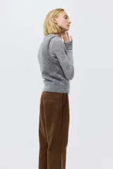 Pantalón de corte bootcut confeccionado en gamuza color marrón. Presenta cierre frontal con botón oculto, bolsillos laterales al bies y costuras decorativas horizontales sobre las rodillas.