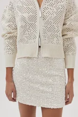 Cárdigan tejido de punto calado color crudo, con cuello polo, cierre metálico frontal y mangas largas.