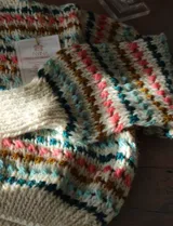 Sweater de punto artesanal, color crudo, con cuello tortuga y diseño de franjas horizontales con detalles en tonos rosado, celeste, verde oscuro y mostaza.