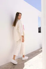 Sobre camisa color crudo, de corte recto, con cuello camisero, cierre frontal con botones y mangas largas con puños abotonados.