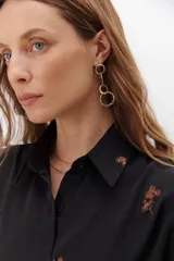 Camisa color crema de tela sedosa bordada con lentejuelas y botones negros a contratono, de corte clásico y mangas largas.