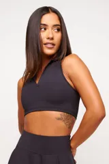 Top deportivo negro, estilo crop top, con cuello polo y escote en V. Presenta tirantes anchos y corte ajustado al cuerpo.